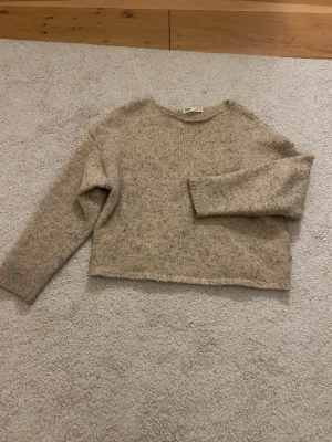 Beige stickad tröja från Pull&Bear - Mysig beige stickad tröja från Pull&Bear i storlek XS. Tröjan har en enkel design med rund hals och lång ärm, perfekt för lager-på-lager under kyliga dagar. Den har en loose passform och är tillverkad i ett mjukt material med diskret melering.