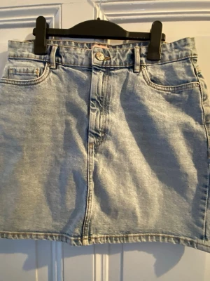 Ljusblå jeanskjol från ONLY, strl 40 - Ljusblå jeanskjol från ONLY i klassisk femficksmodell. Kjolen har bälteshällor, knapp och dragkedja framtill samt två bakfickor. Perfekt till sneakers eller boots.