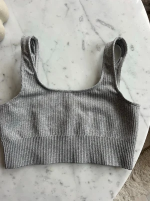 Grå ribbad topp från Aim'n - Snygg grå ribbad topp från Aim'n med breda axelband och fyrkantig ringning. Toppen är stretchig och har en liten metallogo framtill. Perfekt för träning eller som ett basplagg i garderoben.