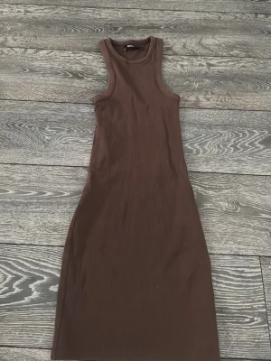 Brun ribbad långklänning Bik Bok - Säljer en brun ribbad långklänning från Bik Bok i storlek S. Klänningen är ärmlös med rund halsringning och har en tight passform som framhäver figuren. Perfekt för dig som gillar en enkel men snygg stil.