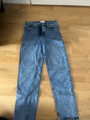 Blå high waist jeans från H&M - Säljer ett par klassiska blå jeans från H&M i storlek 34. De har hög midja, raka ben och femficksmodell. Jeansen är i ett ljusare blått denimtyg och passar perfekt till en avslappnad stil. 