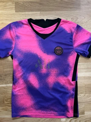 Rosa/lila PSG t-shirt S  -  Jag säljer en PSG t-shirt med fina färger och coolt mönster. Trycket på fram och baksida är utvättat. Trots det passar den bra att ha på gym och under träning. 