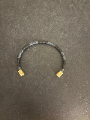 Louis Vuitton svart armband - Säljer ett svart och grått armband från Louis Vuitton med guldfärgade detaljer där loggan syns. Armbandet har en flätad look och känns både stilrent och lyxigt. Perfekt accessoar för dig som vill ha något klassiskt men ändå sticker ut. Skriv om du är intresserad 😁