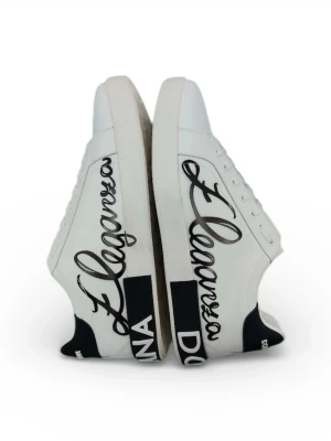 Dolce & Gabbana vita sneakers herr 44 - Säljer ett par vita Dolce & Gabbana sneakers i skinn med svart textdetalj och coolt 'Eleganza' tryck på sidan. Skorna har svarta och vita kontrastdetaljer på hälen och sula med präglad logga undertill. Klassisk rund tå och snörning framtill.
