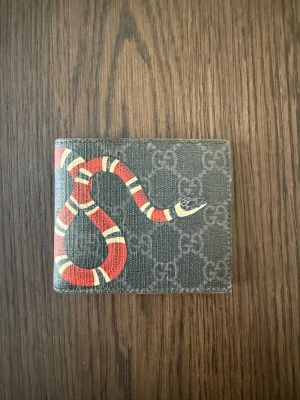 Gucci plånbok  - Säljer en Gucci plånbok i svart med klassiskt GG-mönster och orm. Okej skick finns en liten skada på ett hörn.