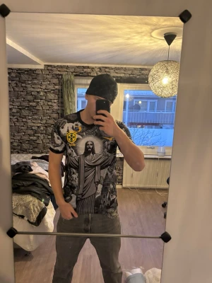 Nike Brasil grafisk t-shirt - Säljer en riktigt fet Nike t-shirt med Brasil-motiv och stora grafiska tryck av Kristusstatyn, byggnader och änglar. Svart och grå bas med inslag av gult och grönt, samt Brasil-logga på bröstet. Perfekt för dig som vill sticka ut med en unik och cool stil.