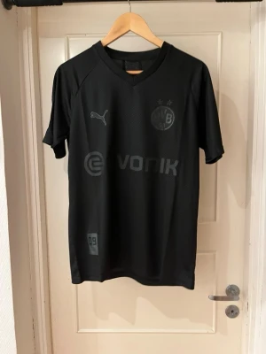 Dortmund special edition 22/23 X Sancho 7 - Säljer en svart Borussia Dortmund tröja från Puma med Sancho och nummer 7 på ryggen. Tröjan har korta ärmar, V-ringning och diskreta tryck i svart och vitt. Perfekt för dig som älskar fotboll och vill ha en stilren supportertröja.