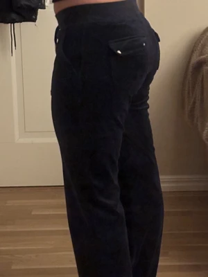 Juicy Couture Byxor - Snygga mörkblå manchesterbyxor med rak passform och snörning i midjan. Byxorna har praktiska fickor både fram och bak, samt silverfärgade detaljer på snörningen. Perfekta för en chill och stilren look.