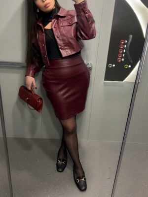 Vinröd set  - Säljer en snygg vinröd kort kjol i skinnimitation med kort jacka. Kjolen har en stilren design utan synliga detaljer och passar perfekt till en trendig outfit. Materialet är mjukt och följsamt, vilket gör den bekväm att bära. Perfekt för dig som gillar att sticka ut med färg och form.Kjol och kort jacka kan tänka mig sälja väskan till vid intresse.Kjolen skulle passa en s-M i storlek och jackan med.