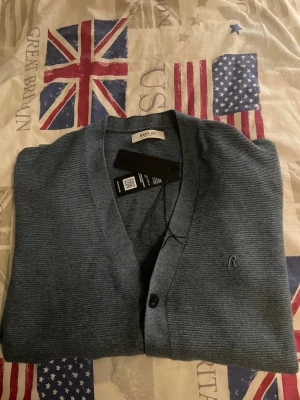 Blå kofta från Replay i ullmix - Snygg blå kofta från Replay med knappar framtill och diskret broderad logga på bröstet. Tillverkad i mjuk material som passar perfekt till lager på lager. Klassisk v-ringad design och långärmad modell. Denna tröja har använts en gång och köptes på NK i Göteborg på självaste Replay butiken väldigt fint och hållbart material.