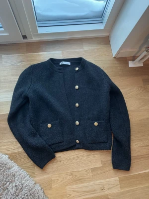 Svart kofta med guldknappar - Stilren svart kofta från zara med raka axlar och dekorativa guldknappar framtill. Två fickor framtill med matchande knappar. Mjuk kvalitet och långärmad modell.