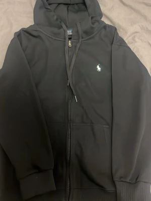 Polo Hoddie  - Perfekt använd några gånger. Gått upp i vikt därför säljer jag den. Svart hoddie med dragkedja av märket Ralph Lauren 