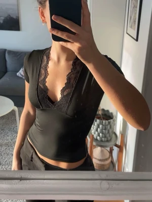 Svart spetsdetaljerad topp Venderby's - Säljer en svart topp från Venderby's i storlek S/M. Toppen har djup v-ringning med breda spetsdetaljer längs urringningen och korta ärmar. Materialet är mjukt och stretchigt, vilket ger en tight passform. Perfekt för dig som gillar stilrena plagg med en twist.