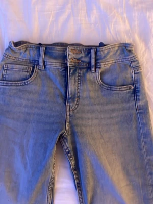 Bootcut ljusblå jeans - Säljer ett par klassiska bootcut jeans i ljusblå tvätt. Jeansen utsvängda ben, fem fickor och knappgylf. Tillverkade i slitstarkt bomullsjeans med snygga kontrastsömmar och silverfärgade knappar. Sitter normalt/medel högt i midjan. Perfekta för dig som gillar tidlös denimstil. Storlek 164 men passar fint på xs/s. Pris går att diskuteras💗
