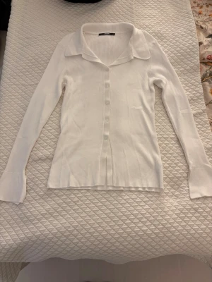 Vit ribbad kofta från BikBok - Vit ribbad kofta från BikBok. Koftan har krage och knäppning framtill med vita knappar. Stretchigt och mjukt material. 