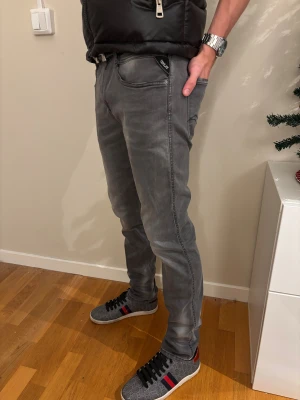 Replay jeans - Säljer ett par grå Replay Hyperflex jeans med snygg tvättad look och klassisk femficksdesign. Jeansen har en slim passform och är tillverkade i stretchigt jeansmaterial som ger skön rörelsefrihet. Märkespatch bak i midjan och diskret broderad detalj på bakfickan.