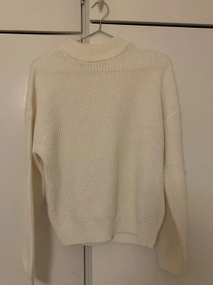 Vit stickad tröja från FB Sister - Säljer en vit stickad tröja från FB Sister i storlek S. Tröjan har en ribbad struktur, hög hals och långa ärmar. Perfekt för kyliga dagar och enkel att matcha med jeans eller kjol. Materialet är mjukt och ger en skön känsla.