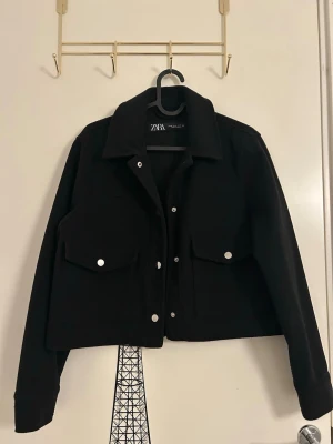 Svart overshirt jacka från Zara - Svart overshirt jacka med klassisk krage, stora fickor och silverfärgade knappar framtill från Zara i storlek XS. Jackan har en croppad passform och långa ärmar med knapp. 
