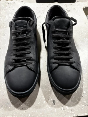 Mörkblå sneakers i skinn - Oliver Cabell  - Säljer ett par stilrena sneakers med rund tå och platt sula. Skorna har klassisk snörning och är tillverkade i slätt skinn med textilfoder. Perfekta för dig som gillar minimalistisk och clean look.