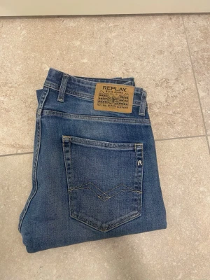 Replay Grover blå jeans, storlek 31 - Säljer ett par Replay Grover jeans i klassisk blå tvätt med raka ben och snygga detaljer på bakfickorna. Jeansen har knappgylf, fem fickor och tydliga Replay-loggor. Perfekt passform och tillverkade i slitstarkt bomullsmaterial.