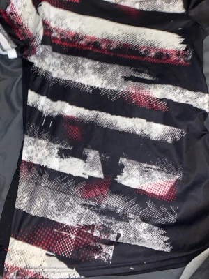 Randig sporttröja från atorka - Säljer en cool sporttröja från Atorka i storlek XS. Tröjan har ett randigt mönster i svart, vit och röd med en grymt grafisk design. Materialet är lätt och syntetiskt, perfekt för träning eller aktivitet. Snygg och modern look med kontrastfärger.