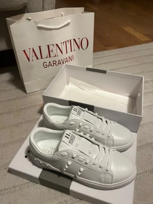 Valentino Garavani Rockstud sneakers - Säljer ett par vita Valentino Garavani Rockstud Untitled sneakers med coola pyramidnitar och snörning. Skorna är i skinn och har en rund tå samt platt sula med mönstrad undersida. Märkeslogga syns både på plösen och innersulan. Perfekt för dig som gillar lyxiga detaljer.