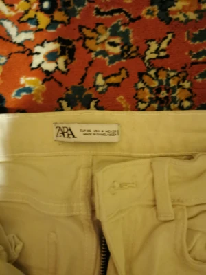 Beiga wide jeans från Zara - Säljer ett par beiga jeans från Zara i storlek 36 med breda ben och råa, fransiga kanter nedtill. Byxorna har klassisk femficksdesign, bälteshällor och dragkedja. Materialet är bomull och passformen är loose för en chill vibe.