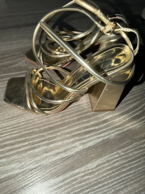 Guldiga sandaler med blockklack - Säljer ett par sandaler i metallic guld med fyrkantig tå och höga blockklackar. Använt på ett bröllop och har varit på hyllan sen dess. Säljs pågrund av flytt