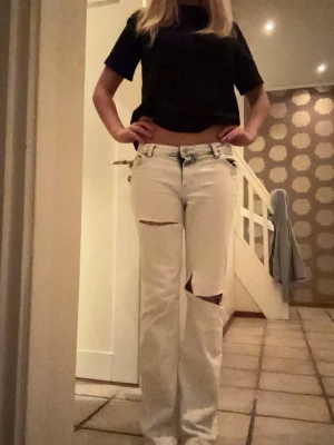 Vita ripped jeans med straight fit - Säljer ett par vita jeans med raka ben och snygga slitningar över knäna. Byxorna har låg midja och klassisk femficksdesign. Perfekt för dig som gillar en avslappnad och trendig stil. Materialet är jeans och passformen är normal.