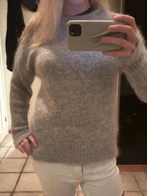 Grå fluffig stickad tröja - Mysig grå stickad tröja med lång ärm och rund hals. Tröjan har en fluffig och mjuk känsla, perfekt för kyliga dagar. Enkel design utan mönster eller detaljer, passar dig som gillar stilrent och comfy.