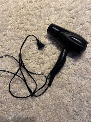 Svart hårfön från BaByliss - En svart hårfön från BaByliss med sladd och klassisk design. Perfekt för att snabbt torka och styla håret. Kompakt modell som är enkel att ta med sig. Tillverkad i plast med tydliga knappar på handtaget. Finns 4 olika lägen🥰