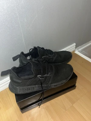 Svarta Adidas sneakers - Säljer ett par svarta Adidas sneakers med klassiska tre ränder på sidan och diskret Adidas-logga på plösen. Skorna har snörning och en platt sula med mönstrad undersida. Ovandelen är i textil och syntet, vilket gör dem riktigt sköna och lätta på foten. Har använts ungefär 1-2 par gånger och kommer inte till användning