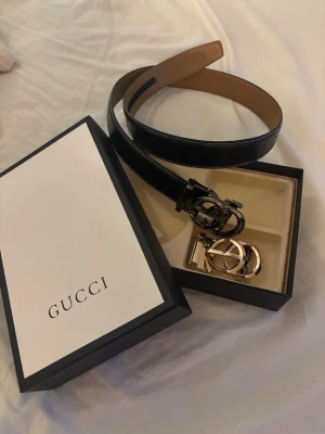 Svart Gucci bälte med GG-spänne - Ett elegant bälte med två utbytbara spännen. Bältet är svart med en distinkt textur.  105cm långt   Obs vet inte om de är äkta eller inte, inget kvitto ingår.