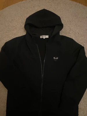 Svart CDG hoodie  - En svart CDG hoodie jättebra skick-finns snöre med men jag har tagit ut de, hör av er vid minsta lilla fråga                                                        