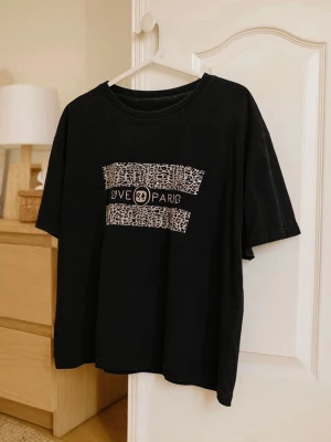 Svart t-shirt med leopardmönster - Cool svart t-shirt från River Island med leopardmönstrad print och text på bröstet. T-shirten har rund hals och korta ärmar, perfekt för dig som gillar streetstyle och djurmönster. Passformen är loose och materialet känns som mjuk bomull.