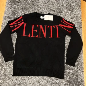 Svart tröja från Valentino  - Svart långärmad tröja från Valentino med stor röd logotyp över bröstet och armarna. Tröjan är tillverkad i 100% bomull och har ribbade muddar vid ärmslut och nederkant. Snygg och stilren design som sticker ut med de röda detaljerna.