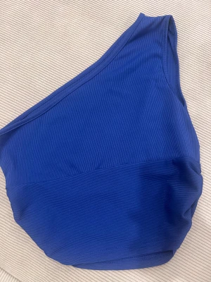 Blå oneshoulder topp från SHEIN - Säljer en snygg blå oneshoulder topp från SHEIN i storlek S. Toppen är ribbad och har en cool asymmetrisk design med en axel bar. Materialet är mjukt och stretchigt, perfekt för att skapa en trendig look.