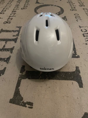 Slalomhjälm - Säljer en vit slalomhjälm från Salomon med grå detaljer och mjuk vaddering på insidan, storlek S. 