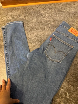 Levi's Slimming Super Skinny Jeans - Snygga blå Levi's jeans i modellen Slimming Super Skinny. Klassisk femficksdesign, normalhög midja och smal passform hela vägen ner. Tillverkade i mjukt och stretchigt jeansmaterial för en bekväm känsla. Perfekta för dig som gillar en tight look.