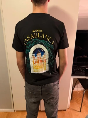 Svart Casablanca t-shirt med tryck - Svart t-shirt från Casablanca i bomull med färgglatt tryck av byggnad och texten 'Avenida Casablanca' på ryggen och mindre tryck på bröstet. Klassisk passform och korta ärmar, perfekt för en chill och stilren look.