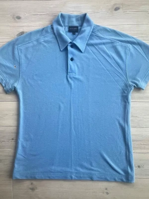 Blå piké från Galvin Green - Säljer en stilren blå pikétröja från Galvin Green i storlek M. Pikén har klassisk krage, två knappar framtill och korta ärmar. Materialet är mjukt och andas, perfekt för varma dagar. Diskret logga på ärmen ger en sportig touch.