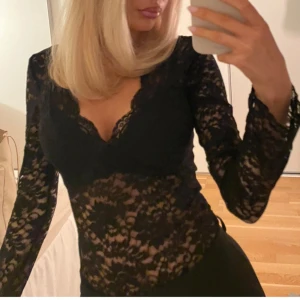 Svart spetsblus med v-ringning - Säljer en svart, långärmad blus i genombruten spets med v-ringad hals och figurnära passform. Blusen har fina spetsdetaljer och är perfekt för dig som vill ha en snygg och trendig look. Passar till både jeans och kjol för en cool outfit.