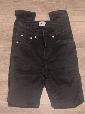 Svarta jeansbyxor från 157 - Svarta jeansbyxor från 157 med klassisk femficksdesign och silverfärgade nitar. Byxorna har dragkedja och knapp framtill, samt bälteshällor. Normal passform. Katt finns i hemmet.