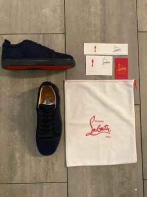 Mörkblå sneakers från Christian Louboutin - Säljer ett par mörkblå sneakers från Christian Louboutin i mocka med den ikoniska röda sulan. Skorna har rund tå, snörning och svarta detaljer. Kommer med originalpåse, box och certifikat. Perfekta för dig som vill sticka ut med exklusiva detaljer. Om ni har några frågor tveka inte att skriva. Kvitto finns !