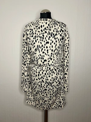 Gepard mönstrad kortklänning från H&M - Säljer en snygg kortklänning från H&M. Klänningen har lång ärm och markerad midja med lätt drapering. Tillverkad i ett mjukt, återvunnet material som känns skönt mot huden. Perfekt för dig som gillar trendiga mönster!