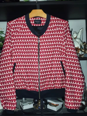 Rödvit hjärt-mönstrad bomberjacka Jascha - Perfekt som present på alla hjärtans dag, till dej eller nån du tycker om. Unik kofta från Jascha Stockholm i storlek S med rödvita hjärtan över hela plagget. Svarta muddar, krage och fickdetaljer samt dragkedja framtill. Insidan är fodrad i svart, vilket ger en snygg kontrast. Perfekt för dig som vill sticka ut! Lämna gärna ett eget prisförslag