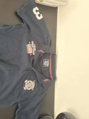 Marinblå piké från Vinson Polo Club - Snygg och klassisk pikétröja från Vinson Polo Club i mörkblå färg. Broderade detaljer på bröstet och ärmen samt randig krage som ger en sportig, tidlös look. Tillverkad i bekvämt pikématerial, perfekt för vardag eller casual stil.                                     J.                                                                        Märke: Vinson Polo Club Storlek: L Färg: Mörkblå Passform: Regular fit Skick: Bra begagnat skick (normalt slitage) Material: Bomull (piké) Perfekt till jeans, 