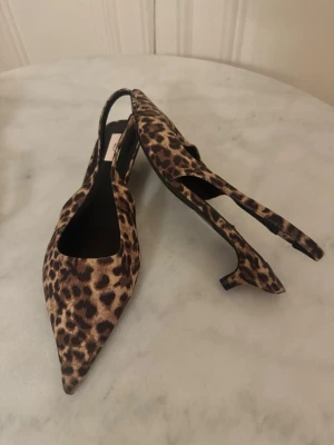 Leopardmönstrade pumps med låg klack - Säljer ett par snygga pumps i leopardmönster med spetsig tå och låg klack. Skorna har öppen häl och är tillverkade i syntetmaterial. 