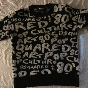 Svart stickad Dsquared2 tröja med text - Cool svart stickad tröja från Dsquared2 med vit text och graffiti-inspirerat mönster över hela plagget.  Tröjan e äkta 100%.                                         Krympte rejält efter tvätt, den känns som xxs ungeefär, 