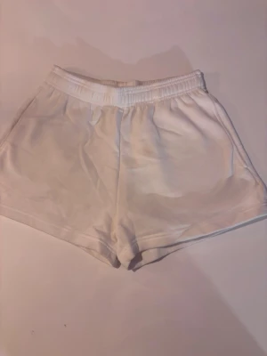 Vita mjuka shorts från Gina Tricot - Vita shorts från Gina Tricot i mjukt material med elastisk midja. De har en enkel och clean design, perfekt för chill dagar eller när du vill ha något bekvämt. Modellen är loose fit och shortsen är enfärgade utan detaljer.